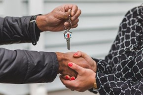 A man giving a house key to a woman with red nails.