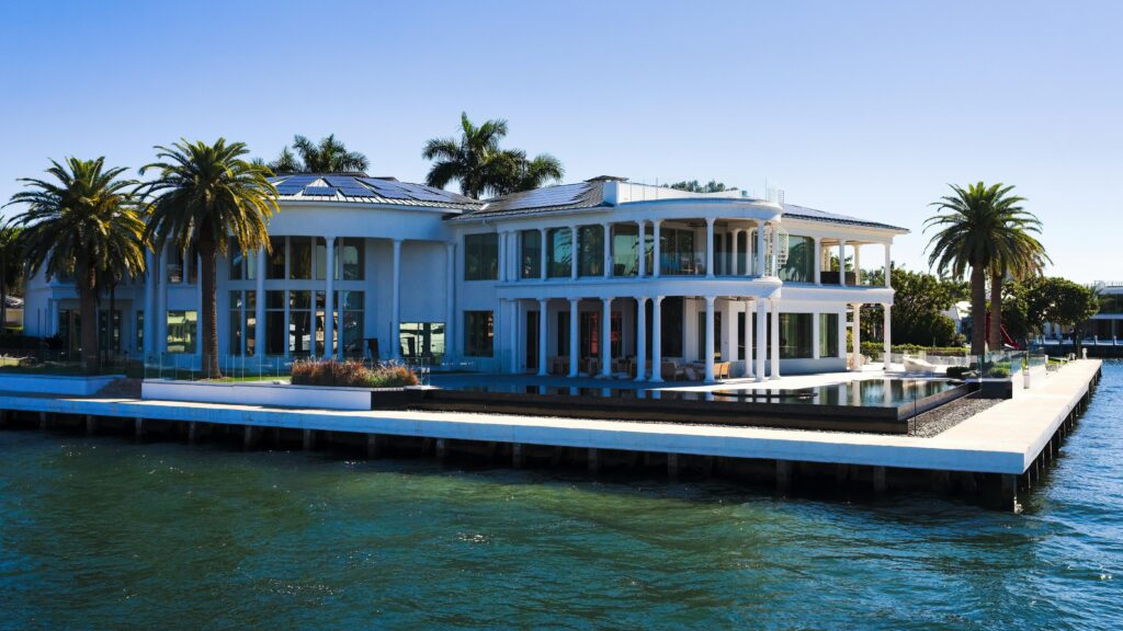 A large white house with a dock and palm trees