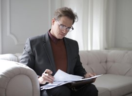 A man in a suit reading a contract while on a white sofa.