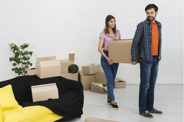 A couple deciding between moving yourself or hiring professionals as they carry moving boxes in a new home.