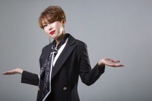 Woman in a business suit with a questioning expression and arms outstretched.