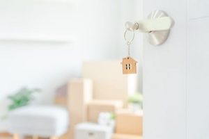 The key is in the door of a new home with moving boxes in the background.